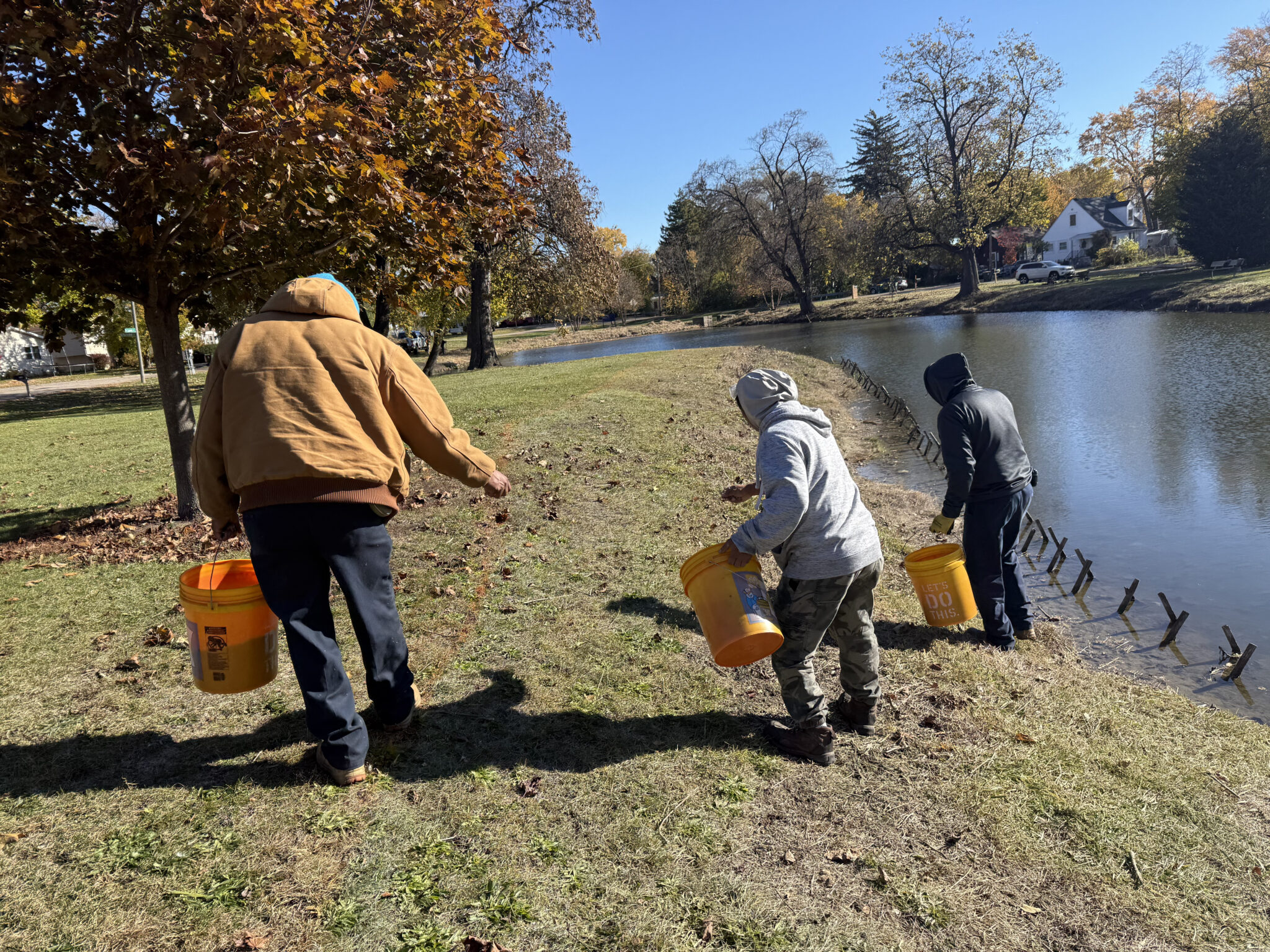 Volunteers carrying buckets while collecting prairie seed beside a pond