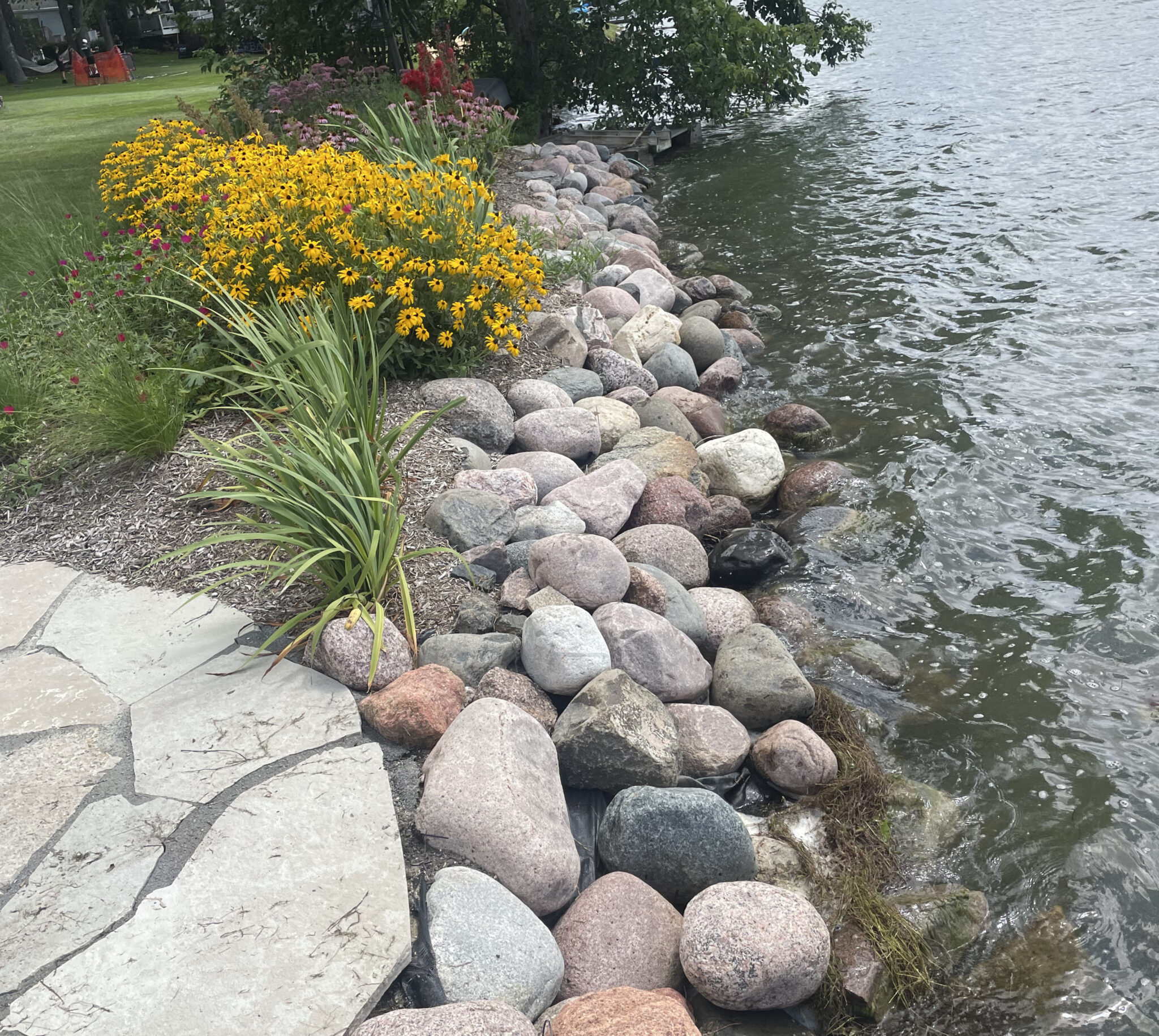 Finished stone shoreline with native grasses and wildflowers at the water's edge