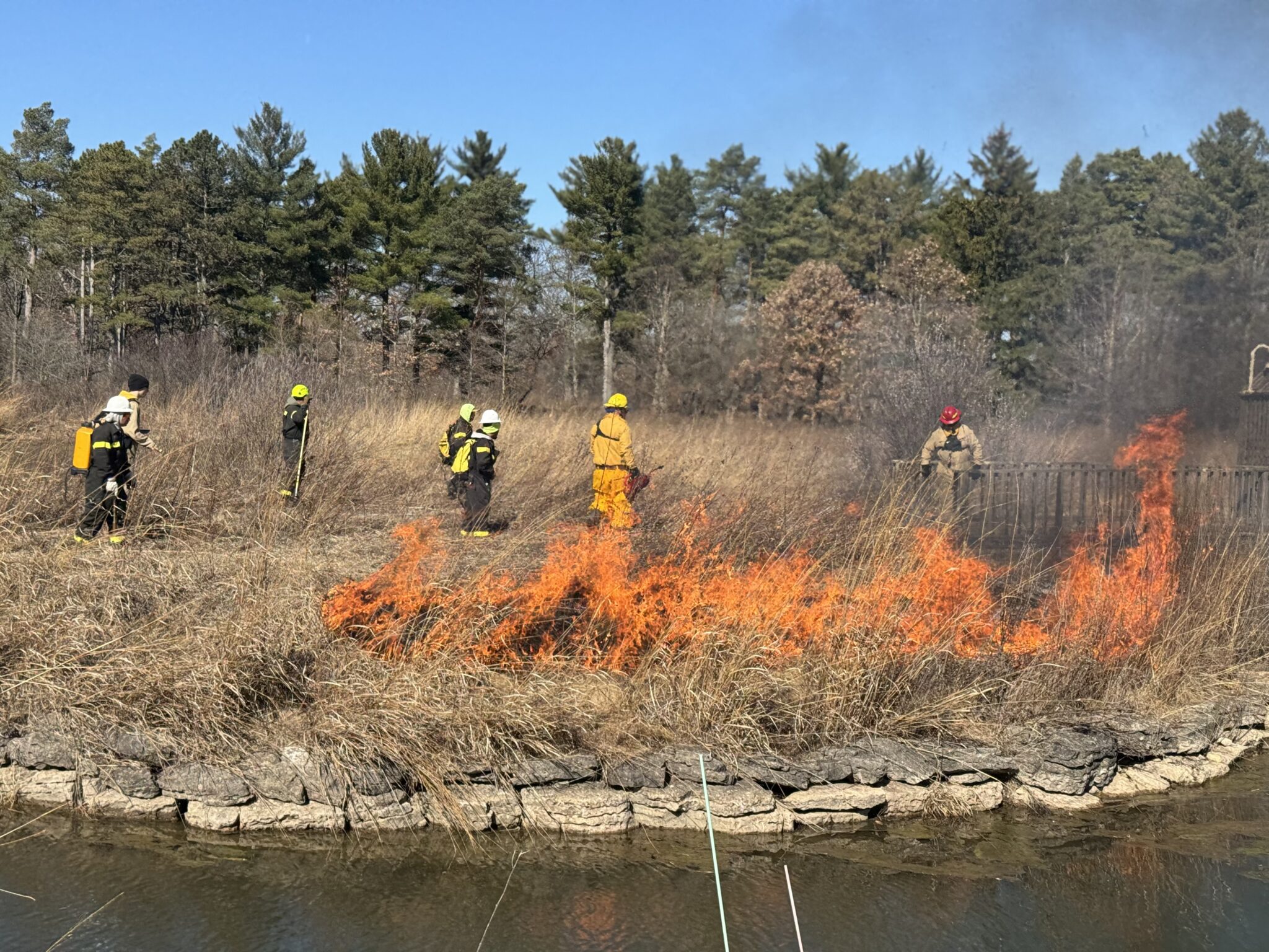 Burn crew in protective gear working a line of fire through dry prairie